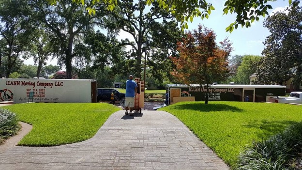 Two ICANN Moving Company trailers at a residential move, a mover wheeling boxes up the walk